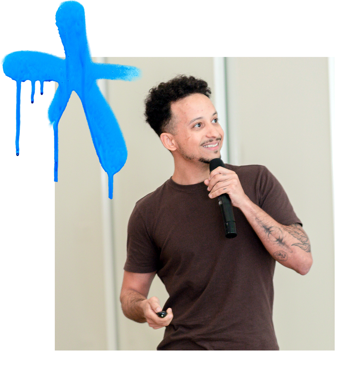 Speaker smiling while presenting, holding a microphone, with a blue graffiti-style paint stroke above him.